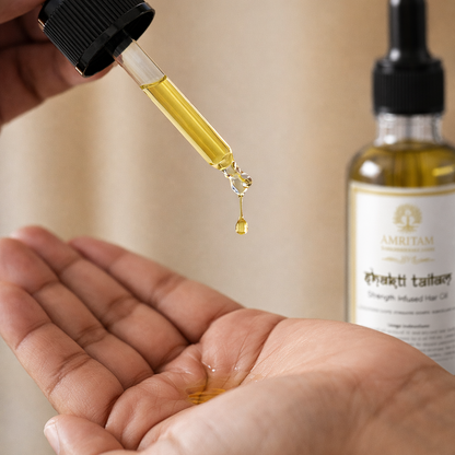 Hand holding a dropper with oil over another hand, with a bottle of oil in the background.